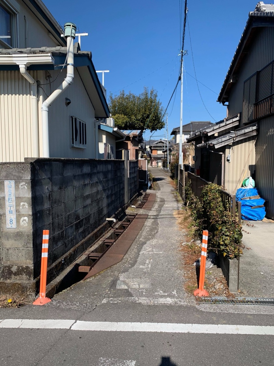 ブロック塀や古い家屋が並ぶ、道幅の狭い路地